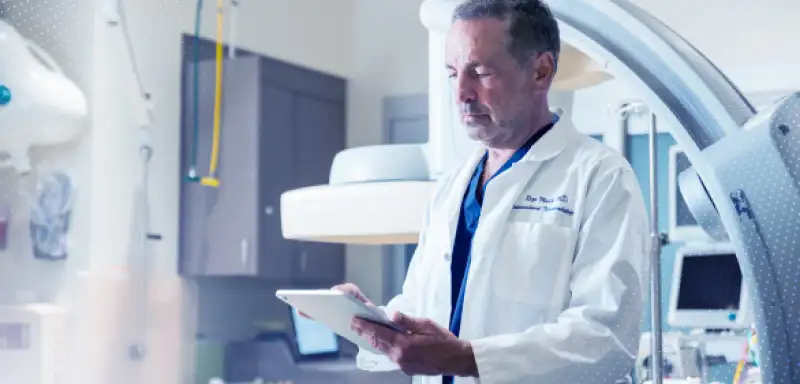 A medical professional in a lab coat holds a tablet, standing in a high-tech hospital environment with medical equipment.